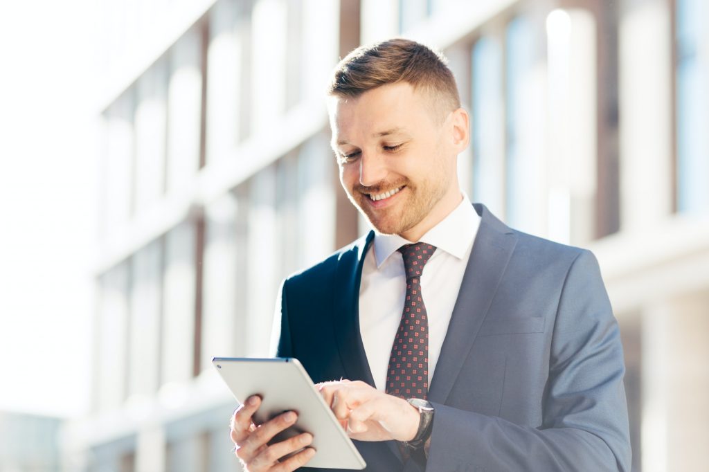Prosperous male entrepreneur searches successful ideas for business in internet, uses modern tablet